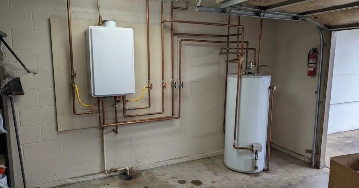 Wall-mounted tankless water heater installed beside existing plumbing in a garage