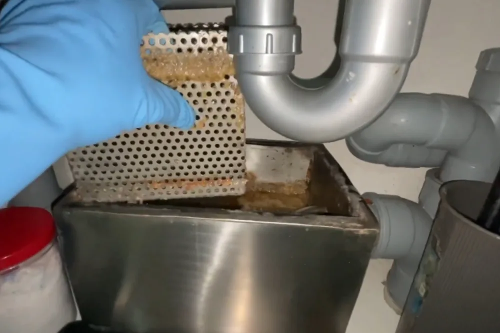 Commercial grease trap basket being lifted out for cleaning
