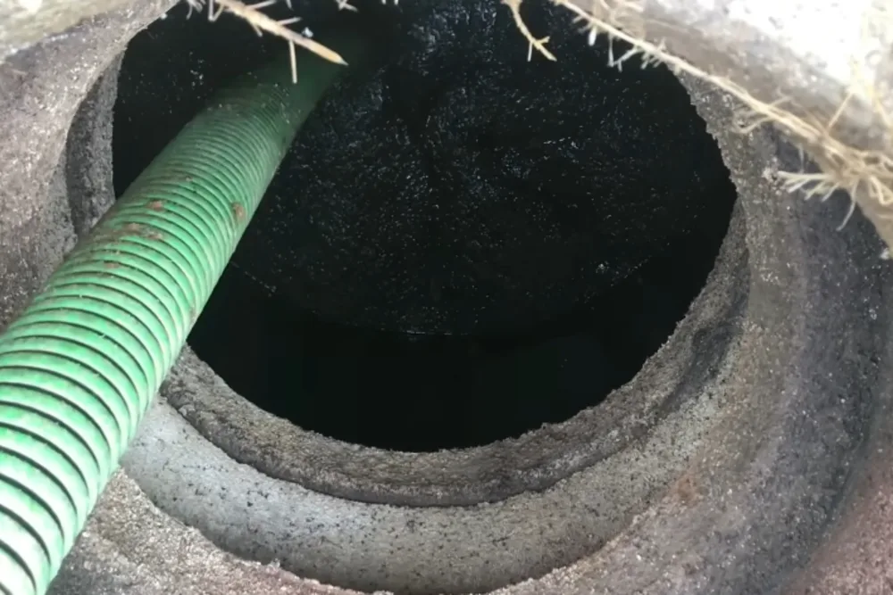 Septic pump truck hose connected to an open tank access port in a lawn