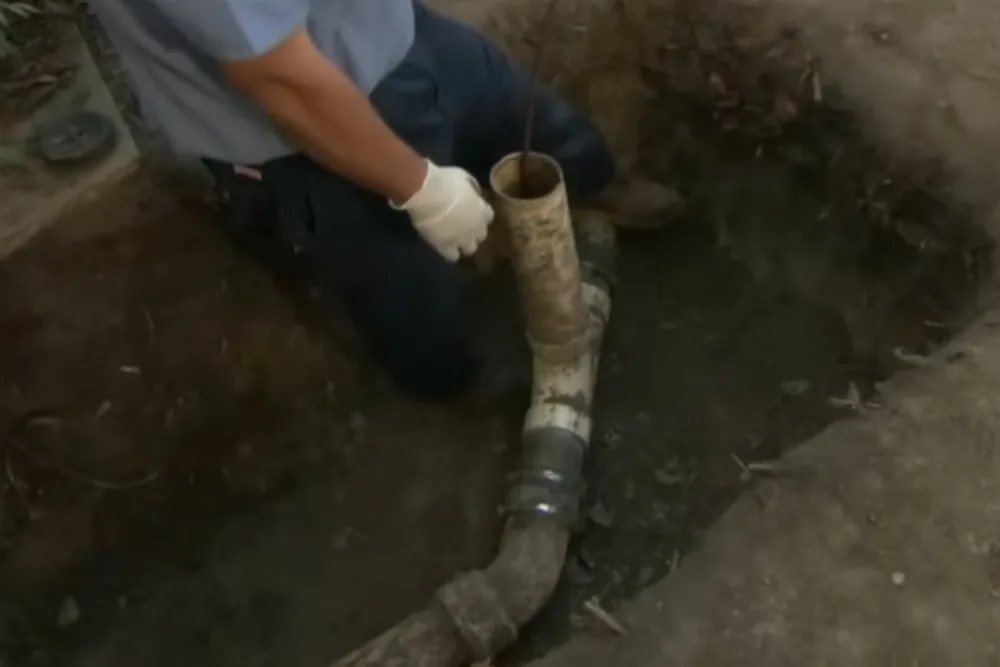 Exposed sewer line section being repaired by a plumber in a crawlspace