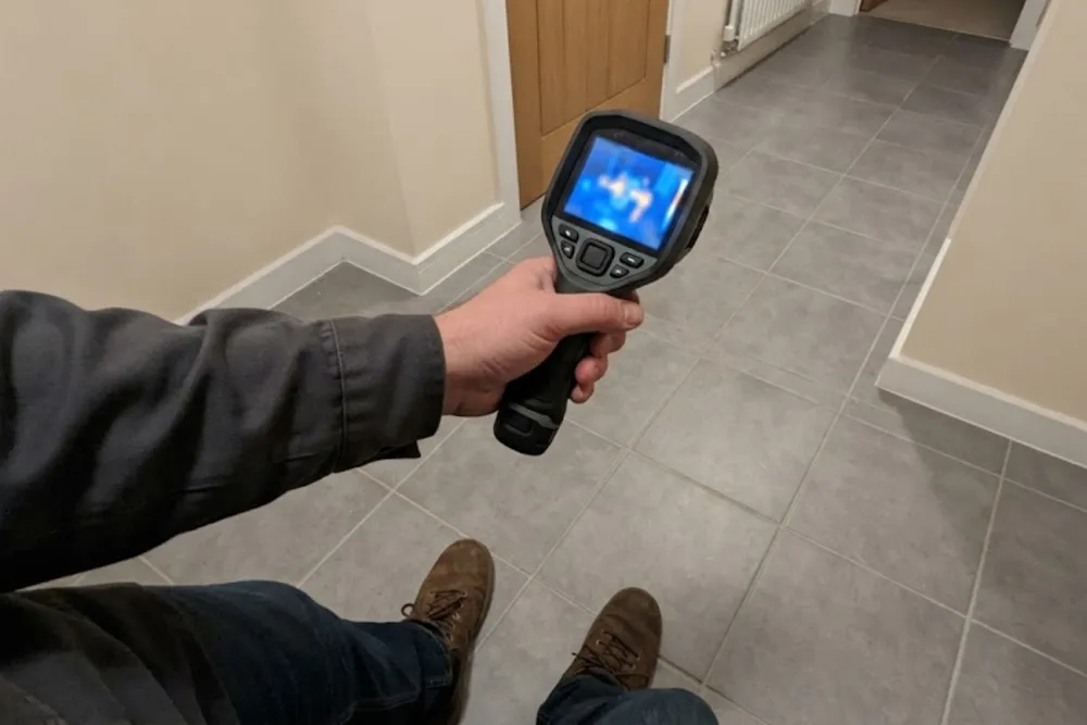 Technician pointing a thermal imaging camera at a tile floor to locate a slab leak