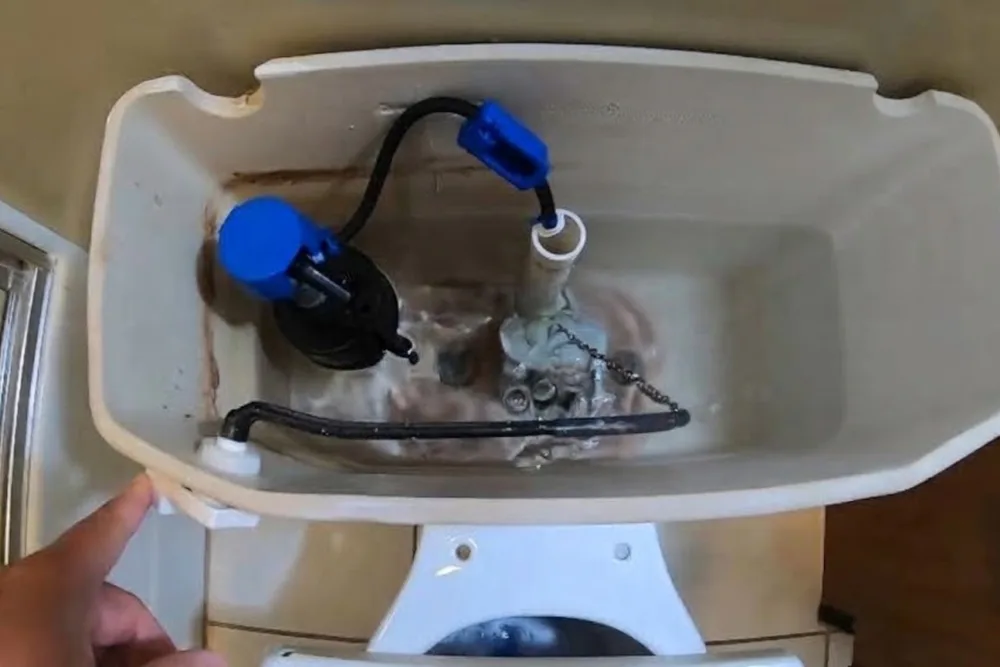 Open toilet tank showing the fill valve and flapper during a repair