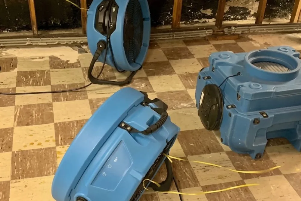 Industrial air movers and a dehumidifier set up to dry a water-damaged room